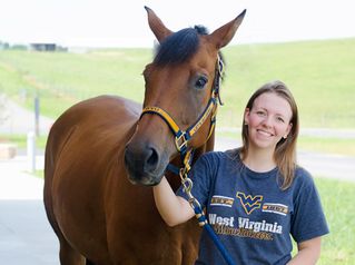 Student in WVU t-shirt standing next to a horse