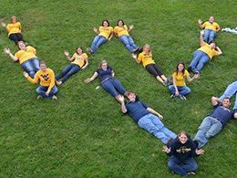 students lying in grass forming the letters WV